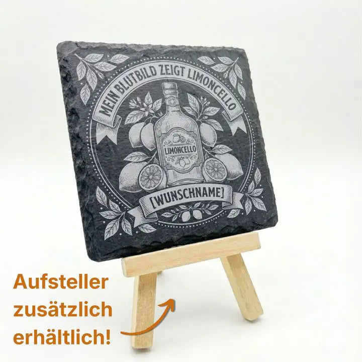 Schieferuntersetzer mit Limoncello-Motiv auf Holzstaffelei mit Hinweis auf optionalen Aufsteller