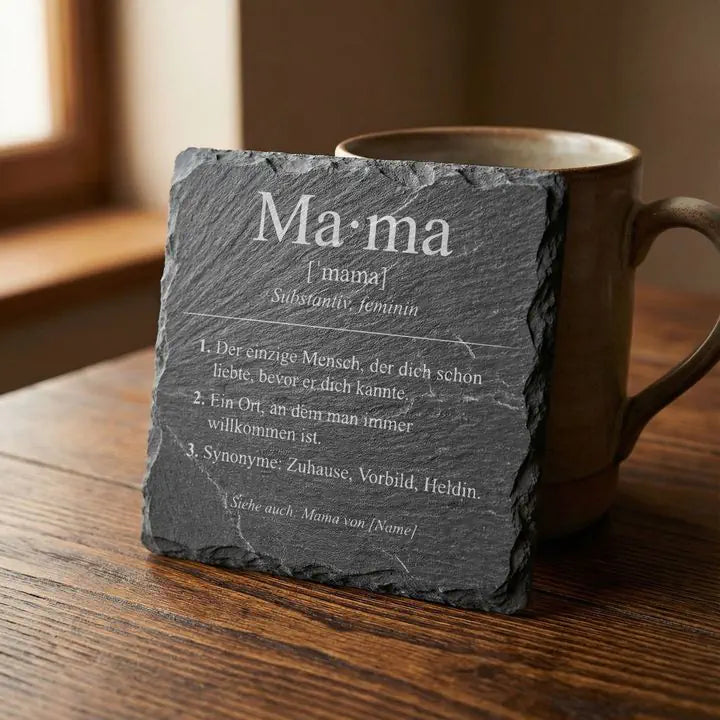 Gravierter Schiefer Untersetzer Mama-Definition lehnt an Keramikbecher auf Holztisch im Tageslicht